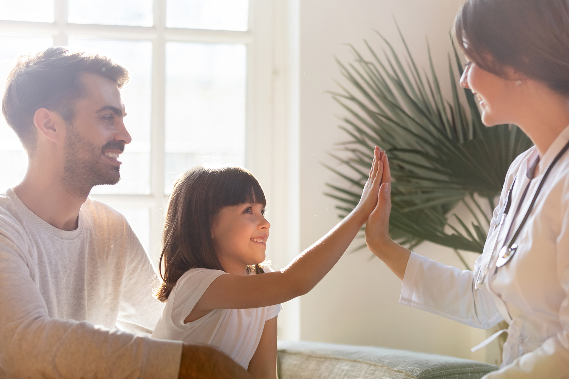 Child high-fiving a doctor beside her father